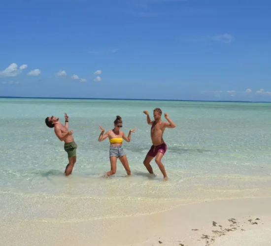 Guests dancing in clear shallow water on a Balabac sandbar